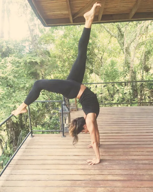 Postura invertida em um deck de madeira no meio da mata.